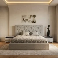تخت خواب رایکا در فضای اتاق خواب مدرن، هدبورد طوسیِ لوزیدوزیشده در مرکز دیوار و چیدمان روتختی کرم و بالشهای طرحدار، همراه با پاتختیهای کناری و فرش روشن در کنار پنجره بزرگ